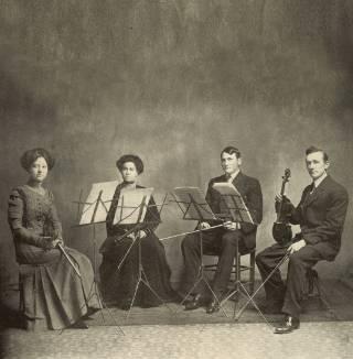 四个1911年的学生音乐家拿着乐器摆姿势拍照
